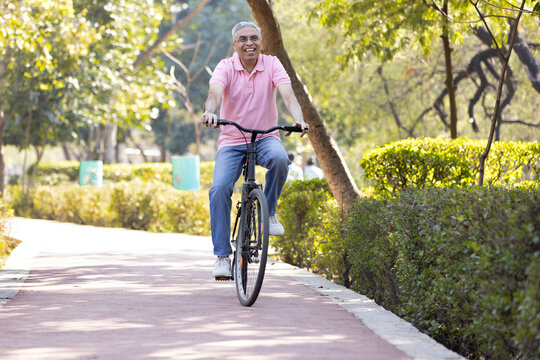 Cheerful senior man having fun riding bicycle at park