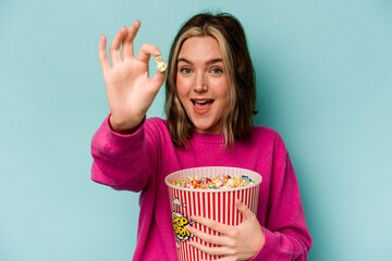 Young caucasian woman holding popcorn isolated on blue background