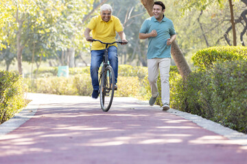 Cheerful senior man riding bicycle while son running at park