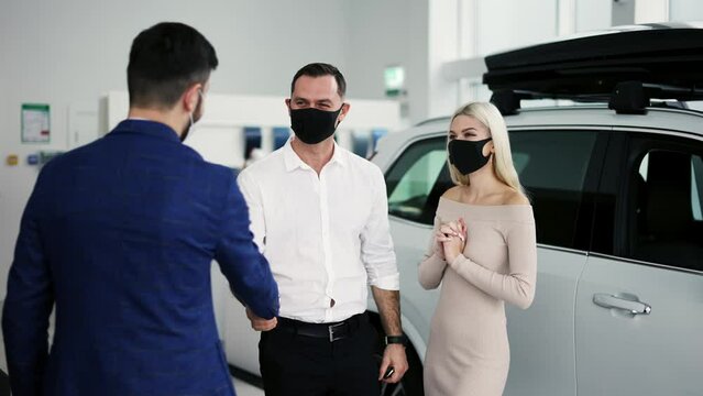 New car owners getting keys to purchased luxury auto in dealership, wearing masks