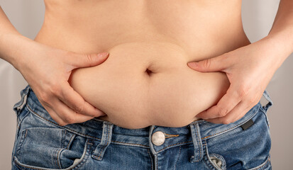 Naklejka premium Woman hands pinching her excess belly fat. Obese woman hand holding excessive belly fat, Overweight fatty belly of woman