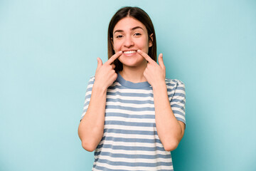 Fototapeta premium Young caucasian woman isolated on blue background smiles, pointing fingers at mouth.