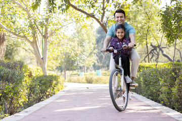 Young man riding bicycle with daughter at park