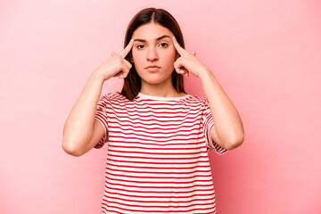 Young caucasian woman isolated on pink background focused on a task, keeping forefingers pointing head.