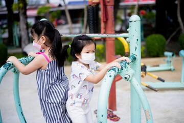 Portrait two kids girl stand and play with their backs facing each other. Cute children wear face mask while outside to prevent spread of respiratory tract virus and PM2.5 particulate matter.