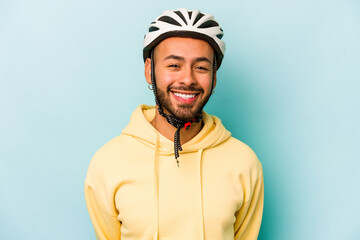 Young hispanic man wearing helmet isolated on blue background laughing and having fun.