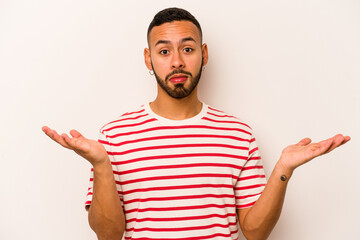 Young hispanic man isolated on white background doubting and shrugging shoulders in questioning gesture.