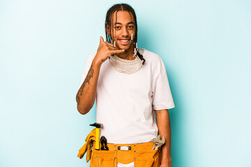 Young mechanic African American man isolated on blue background showing a mobile phone call gesture with fingers.