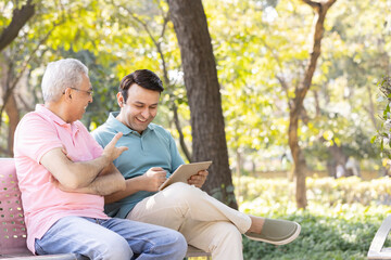 Senior man with son watching social media content on digital tablet at park