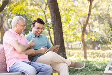 Senior man with son watching social media content on digital tablet at park