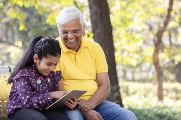 Senior man with granddaughter having fun watching digital tablet at park