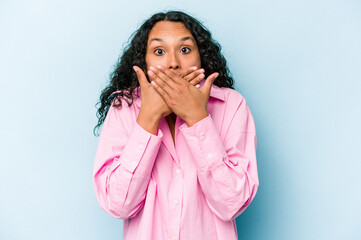 Young hispanic woman isolated on blue background shocked covering mouth with hands.