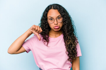 Young hispanic woman isolated on blue background showing a dislike gesture, thumbs down....