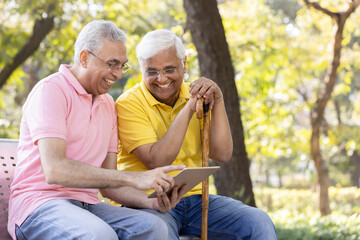 Two senior male friends watching social media content on digital tablet at park