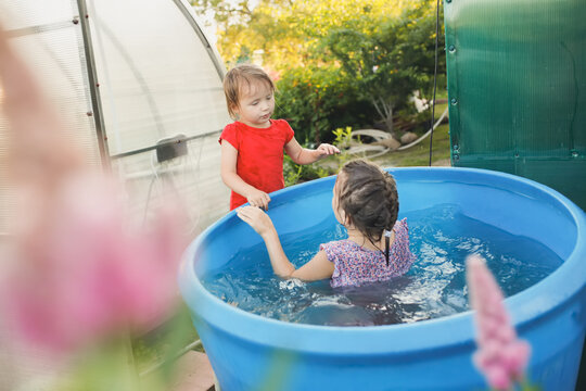 Three sibling children, three sisters bathe in a large barrel in the backyard of the house. Hot summer and happy childhood. Freshness summer heat in the garden