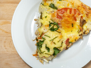 A piece of pizza with cheese, herbs and tomatoes on a white plate on the table. Delicious homemade food.