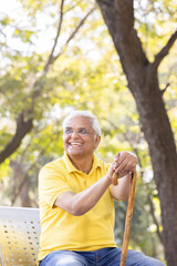 Cheerful senior man sitting on bench with walking stick at park