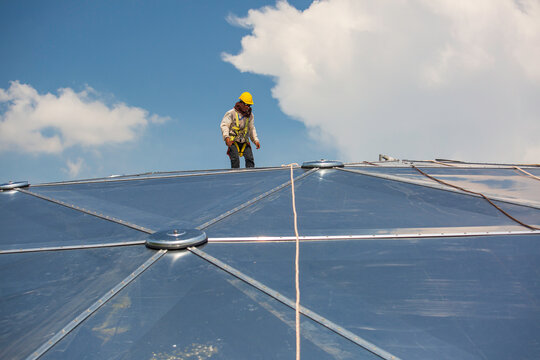 Male workers rope access height safety connecting with a knot safety harness, clipping into roof construction site oil tank dome