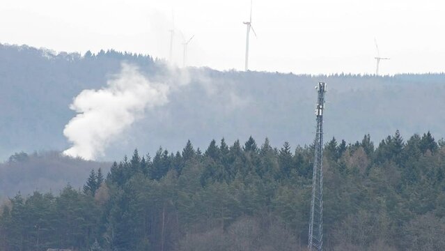 Small forest fire in front of several wind turbines on the top of a mountain ridge in Germany. Static compressed view