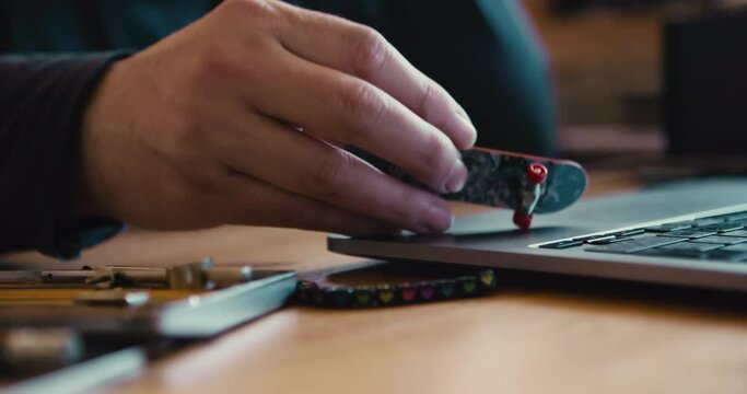 Procrastination and unwillingness to work. A man plays with a small toy skateboard on the body of a laptop. Close-up shot of hand with a toy.