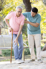 Young man helping and supporting his father in walking at park