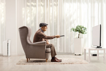 Elderly man in an armchair changing channels on TV with remote control in a living room