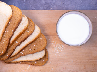 Pieces of rye and white bread with a glass of milk on a kitchen board.  Bakery products with sesame seeds.