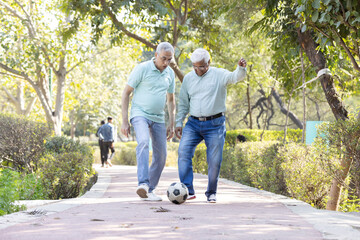 Obraz premium Two senior man having fun while playing football at park