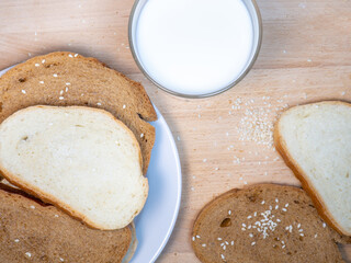 Naklejka premium Pieces of rye bread with a glass of milk on a kitchen board. Bakery products with sesame seeds.