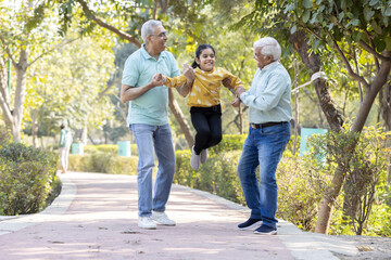 Obraz premium Two cheerful senior men having fun while playing with granddaughter at park