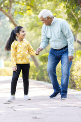 Senior man holding stick while walking with granddaughter at park