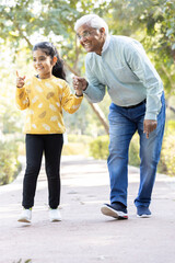 Obraz premium Senior man holding stick while walking with granddaughter at park