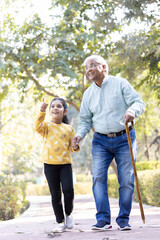 Senior man holding stick while walking with granddaughter at park