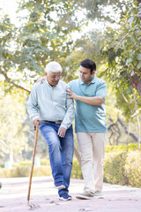 Obraz premium Young man helping and supporting his father in walking at park