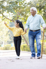 Obraz premium Senior man holding stick while walking with granddaughter at park