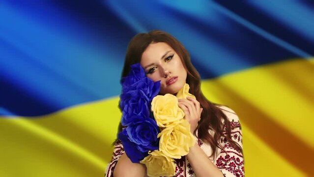 a woman in national clothes looks into the camera with love and anxiety because of the escalation of the military conflict in Ukraine, the Russian invasion against the background of the flag of Ukrain