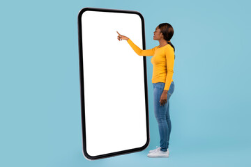 Smiling pretty young african american woman reading message on empty screen of huge smartphone