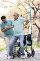 Fototapeta na wymiar Young man assisting a senior man in a wheelchair at park