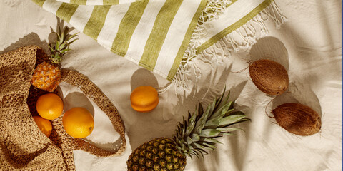 Fresh oranges, pineapple, coconuts falling out from woven bag on sandy beach. Tropical holiday...