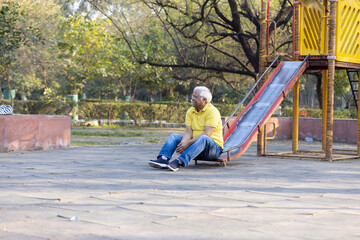Cheerful senior man sliding in playground at park