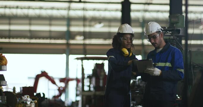UntitleIndustrial engineer, technician worker wearing uniform, safety hard hat using tablet computer checking control automated robotic arm machine in factory. Automatic manufacturing