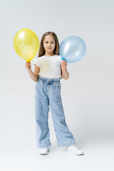 Fototapeta premium full length view of ukrainian girl in jeans standing with blue and yellow balloons on grey.