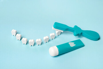 A toy tube of toothpaste and a toothbrush with a model of teeth standing in the shape of a smile....