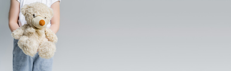 partial view of child holding teddy bear isolated on grey with copy space, banner.