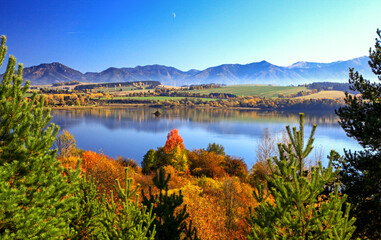 Autumn trees and mirror reflection of mountains in lake