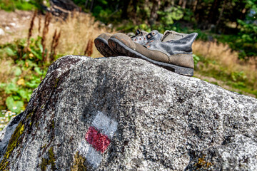 Old used hiking boots and tourist sign on rock