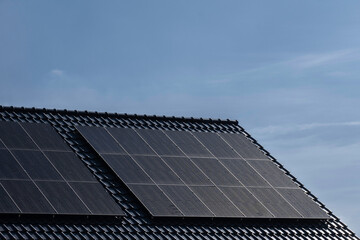 Solar panels mounted on the tile roof of a modern new-build house in the Netherlands with blue sky. Sustainable energy