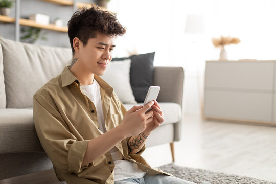 Smiling asian man using cellphone at home sitting on floor