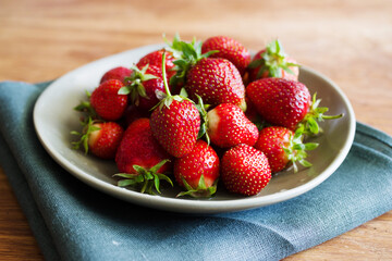 Fresh juicy strawberries in a plate on a wooden table surface, closeup. Summer berry harvest