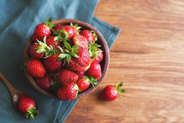 Fresh juicy strawberries in a plate on a wooden table surface, top view, copy space. Summer berry...